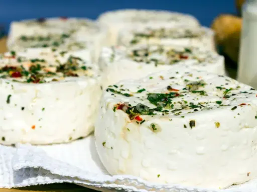 Kilka okrągłych serów labneh z ziołami i przyprawami na białej serwetce.