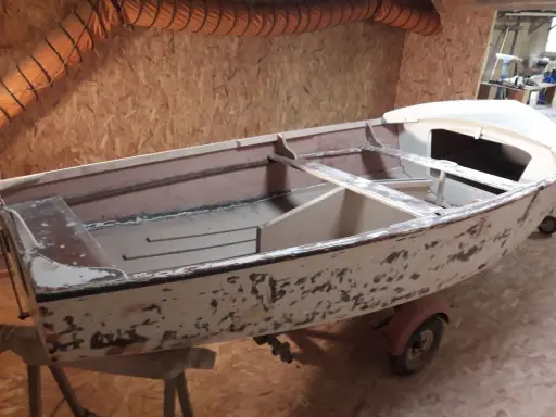 Un dériveur Caravelle polyester en cours de restauration, sur sa remorque. La coque est décapée, prête pour une nouvelle peinture.