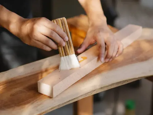 Un artisan ébéniste applique une finition sur un morceau de bois avec un pinceau.