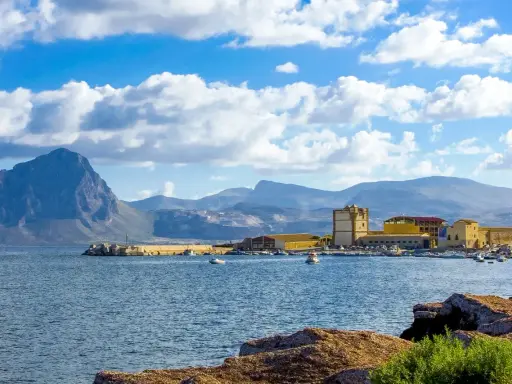 La tonnara di Bonagia, con il suo porto e le montagne sullo sfondo, sotto un cielo azzurro e nuvoloso.