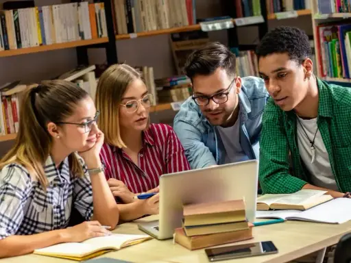 Studenci pochłonięci nauką historii przy laptopie w bibliotece.