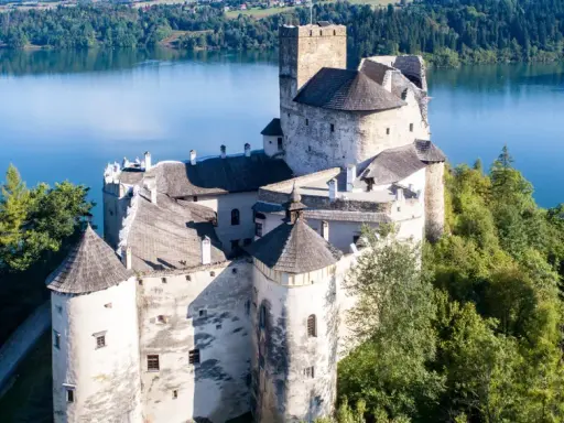 Zamek Dunajec, majestatyczna twierdza na skale, otoczona zielenią i błękitną wodą jeziora.