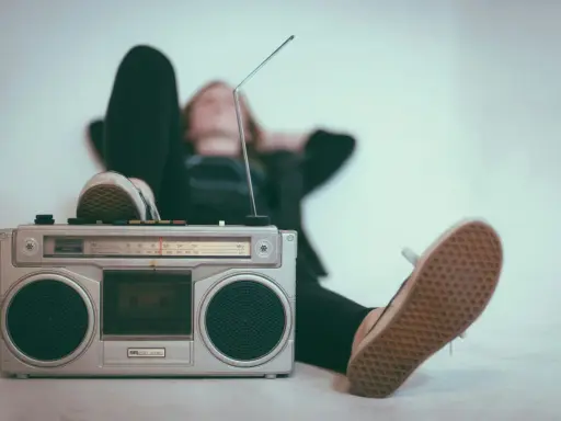 Osoba relaksuje się przy radiomagnetofonie, słuchając muzyki. To pokazuje, jak łatwo dotrzeć do odbiorców, co jest jedną z **zalet reklamy radiowej**.