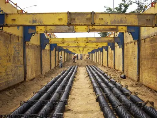 Trabajadores instalan tuberías en una zanja profunda, con estructuras metálicas amarillas para entibar zanjas y prevenir derrumbes.