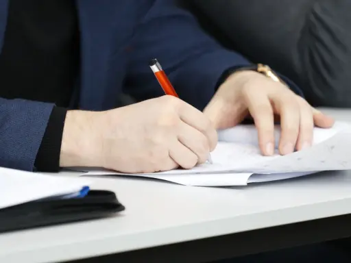 Ręka pisze długopisem po papierze, przygotowując przykładowy artykuł po angielsku na maturę.