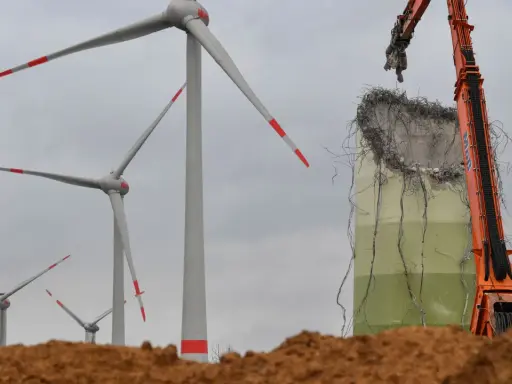 Abrissbagger demontiert eine Windkraftanlage. Im Hintergrund stehen noch weitere Windräder, die ihre lange Laufzeit hinter sich haben.