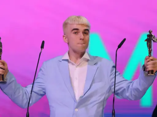 Mc Mata z dwoma statuetkami na scenie, w jasnoniebieskiej marynarce i białej koszuli.