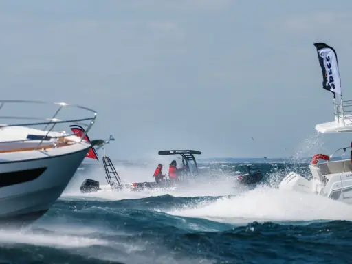 Trois bateaux en pleine navigation, éclaboussures d'eau, ciel bleu. L'un d'eux, un Zodiac, fend les vagues avec deux personnes à bord.