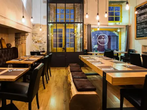 Ambiance chaleureuse au restaurant "Les Fougeres". Tables en bois brut, banquette en cuir et cheminée imposante créent un décor rustique et élégant.