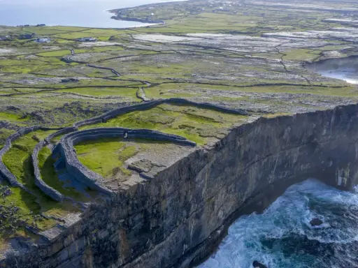 Steile Klippen und alte Steinmauern auf einer grünen Insel vor Galway, Irland. Wellen schlagen gegen die Felsen.