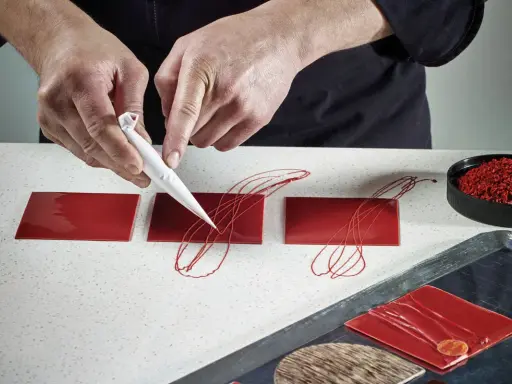 Mains travaillant avec du chocolat plastique rouge pour décorer des carrés de glaçage.