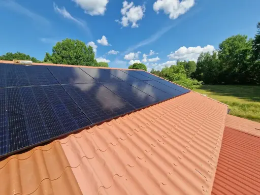 Solceller på ett tegeltak, redo för besiktning. Solen skiner på de mörka panelerna mot en blå himmel med vita moln.