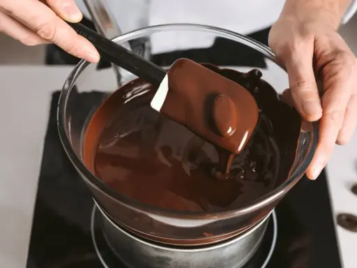 Un chocolat qui ne fond pas ? Ce n'est pas le cas ici ! Une spatule mélange du chocolat fondu brillant dans un bol en verre au-dessus d'un bain-marie.