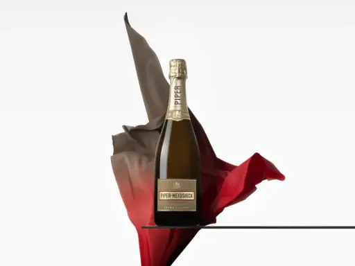 Eine Flasche Piper Heidsieck Cuvée Sublime, umhüllt von fließenden roten und braunen Stoffen, auf einer Glasplatte.