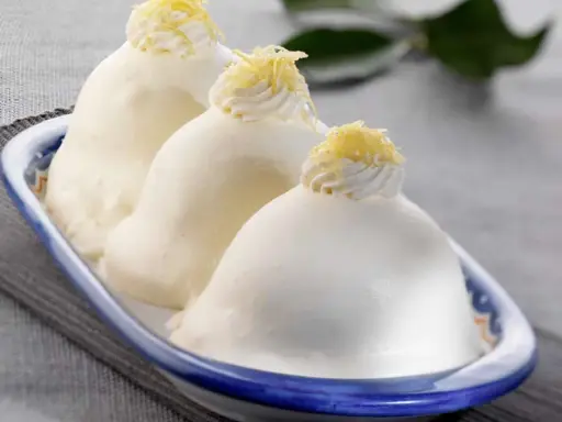 Tre deliziose delizie al limone, guarnite con panna e scorza di limone, in un piatto blu e bianco.