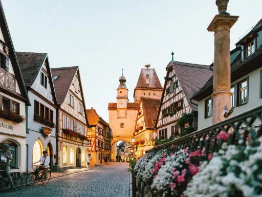 A charming street in gay Germany, with historic buildings, cobblestones, and flowers. Two people on bikes pause to take in the view.