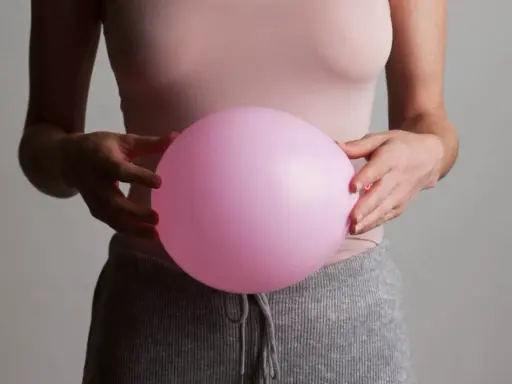 En person håller en rosa ballong mot magen, som om den vore uppsvälld och gör att personen känner sig dålig i magen.