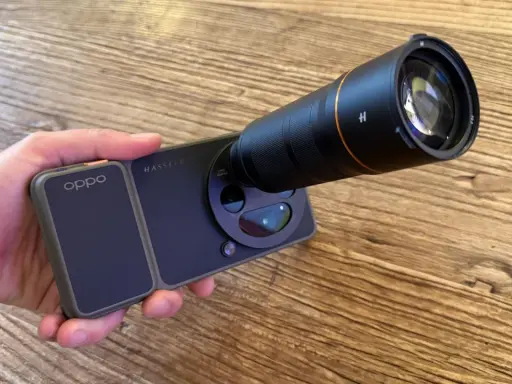 Mano sujetando un teléfono **cámara Oppo** con un gran lente acoplado, listo para capturar imágenes detalladas.