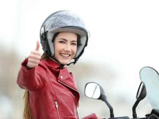 Mujer sonriente con casco y chaqueta roja, pulgar arriba. ¡Sacarse el carnet A2 es más fácil de lo que parece!