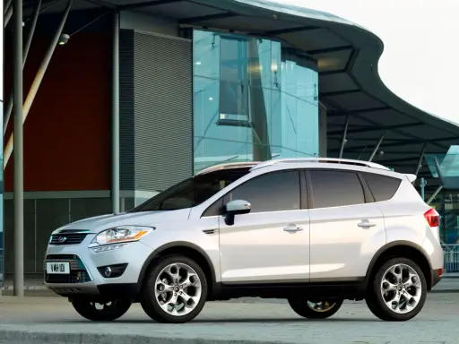 Biały Ford Kuga 2010 zaparkowany przed nowoczesnym budynkiem z przeszkloną fasadą.