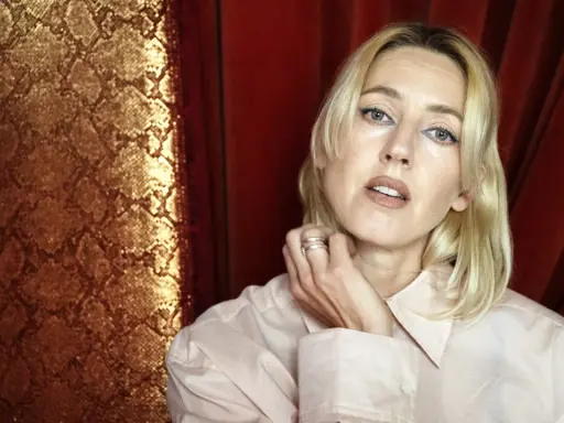 Veronica Maggio ung, med blont hår och blå eyeliner, poserar framför en gyllene ormskinnsmönstrad bakgrund och röda draperier.