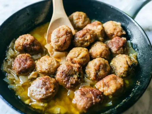 Polpette in bianco cremose in padella, dorate e succulente, adagiate su un letto di cipolle caramellate.