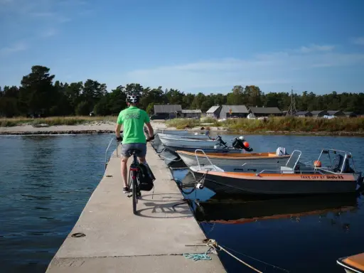En cyklist på en brygga med båtar vid en svensk kust. Perfekt för att utforska cykelleder Sverige.