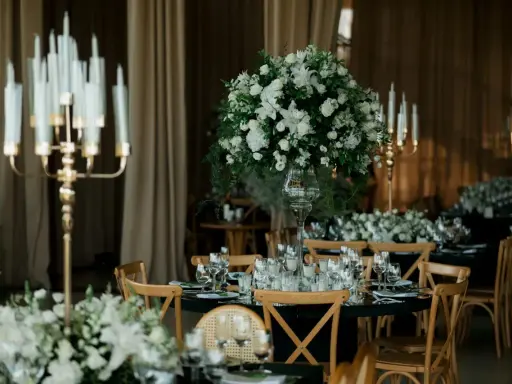 Eleganckie wesele w czarnym stylu. Stoły nakryte czarnymi obrusami, ozdobione białymi kwiatami i złotymi świecznikami.