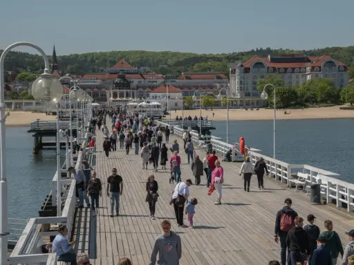 Tłum ludzi spaceruje po molo w Sopocie, jednym z najpopularniejszych gdańsk atrakcje. W tle widać plażę i zabytkowe budynki.