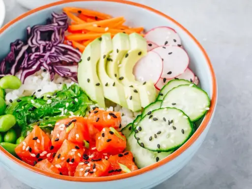 Eine bunte Poke Bowl mit Lachs, Avocado, Edamame, Rotkohl, Gurke, Radieschen und Seetang.