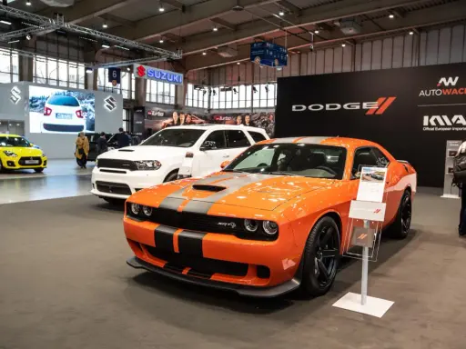 Pomarańczowy Dodge Challenger Hellcat z szarymi pasami na masce, obok białego SUV-a Dodge Durango.