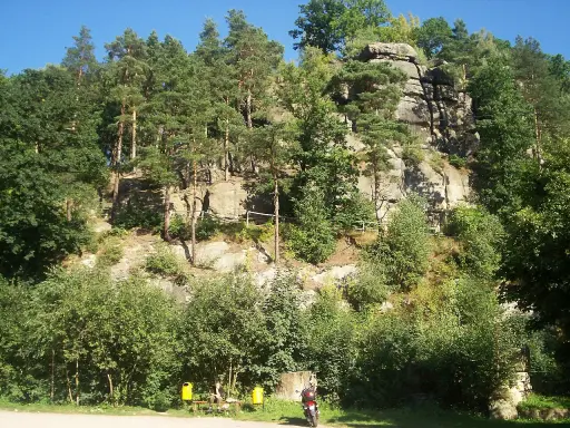 Skały i lasy tworzą malowniczy krajobraz, przypominający szwajcarię lwówecką. Na pierwszym planie motocykl i ławka z siedzącą osobą.