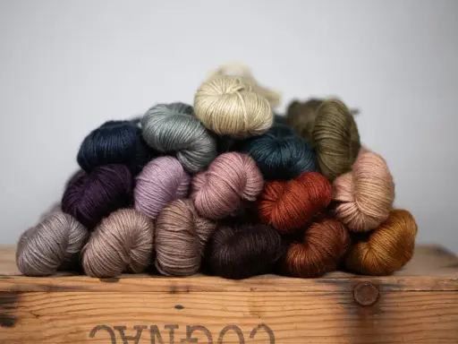 A pile of colorful yarn skeins in various earthy tones, resting on a wooden crate.