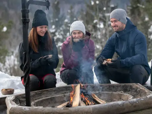 Vänner njuter av värmen från en eld och fika under härliga ute aktiviteter i snöig skogsmiljö.