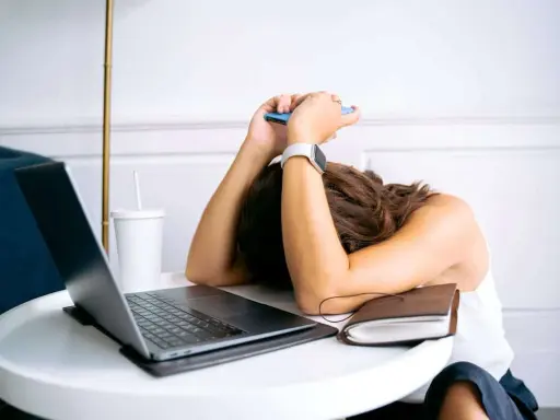 Personne épuisée, tête sur les bras, téléphone à la main, devant un ordinateur portable. L'effet écran de la fatigue est palpable.