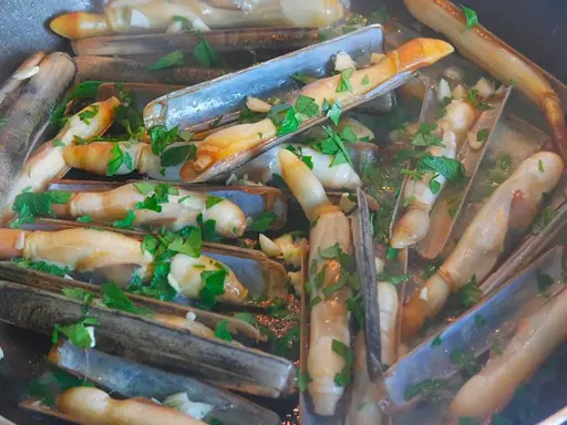 Couteaux en persillade cuits dans une poêle, parsemés de persil frais. Un plat savoureux et simple.
