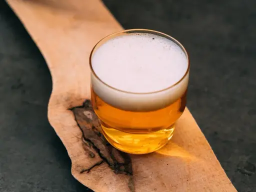 Szklanka złocistego piwa z białą pianką, prezentująca standardową dawkę alkoholu, stoi na drewnianej desce.