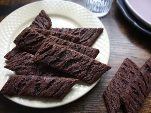 Chokladsnittar recept: Mörka, avlånga chokladkakor med räfflad yta ligger på en ljusgul tallrik. Perfekta till fikat!