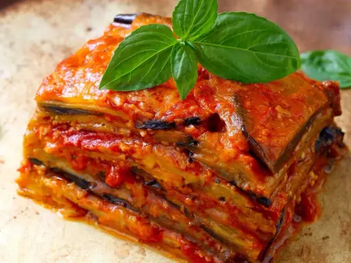 Une part généreuse d'aubergine parmigiana, empilée et nappée de sauce tomate, garnie de feuilles de basilic frais.