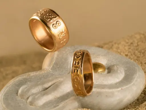 Due anelli d'oro con incisioni uniche, che mostrano diversi tipi di fedi nuziali, su una pietra a forma di mano con sabbia.