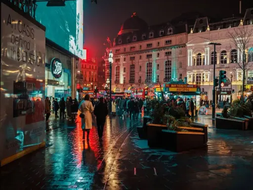 Luci al neon e riflessi sull'asfalto bagnato, la vibrante vita notturna londra pulsa tra la folla e gli edifici storici illuminati.