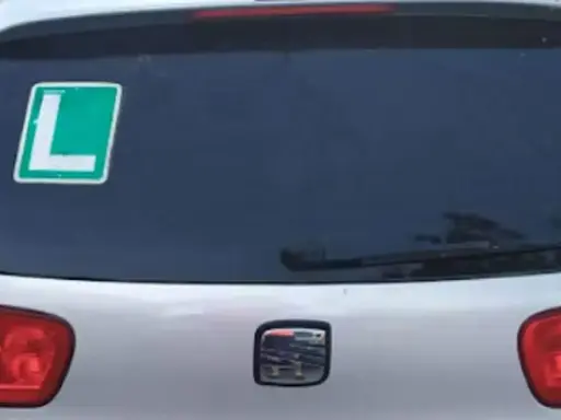 El coche tiene una L verde en la ventana trasera, indicando que el conductor está aprendiendo.