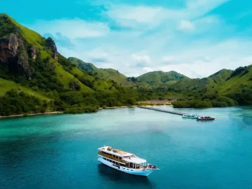 Un'isola lussureggiante con colline verdi e un mare turchese, dove si trova Bali, con una nave da crociera che naviga nelle acque cristalline.