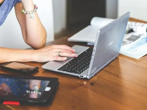 Nauczycielka pracuje na laptopie, który może być zakupiony dzięki bonowi na laptopa dla nauczycieli. Obok leżą tablet i telefon.