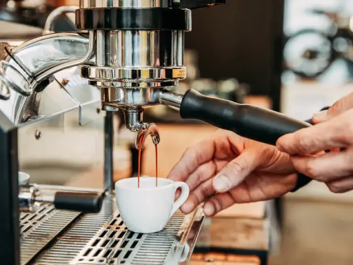Frisch gebrühter Kaffee fließt aus der Espressomaschine in eine kleine Tasse.