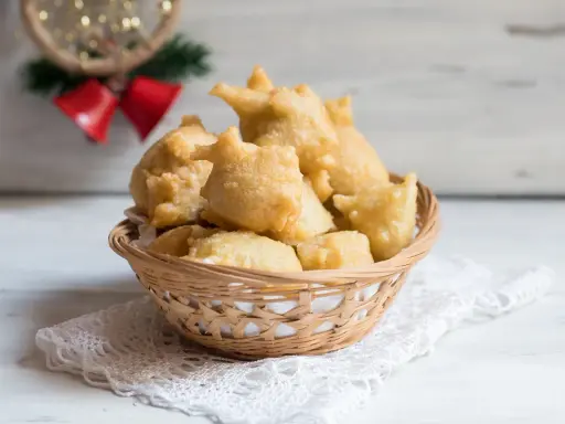 Cesto di pittula salentina dorata, un dolce fritto tipico delle feste, su un pizzo bianco.