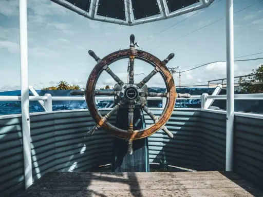 Roue de gouvernail en bois patiné, prête à barrer un bateau vers l'horizon bleu.