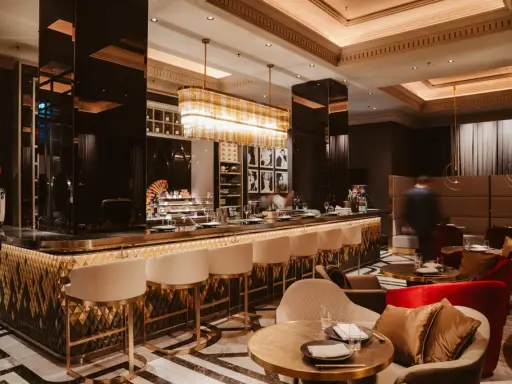 Elegante Bar mit goldenen Akzenten, weißen Barhockern und stilvollen Sitzbereichen. Ein Ort, der zu den besten Restaurants in Berlin passt.