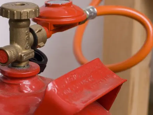 Détail d'une bouteille de propane rouge avec détendeur et tuyau orange, illustrant la norme d'installation gaz propane bouteille.