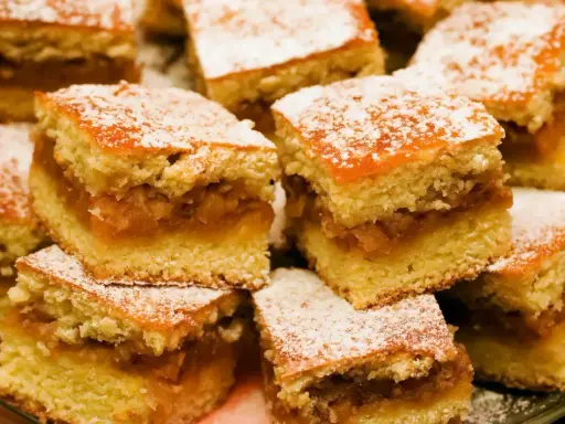Pyszny jabłecznik na biszkopcie, posypany cukrem pudrem, kusi swoim domowym wyglądem.